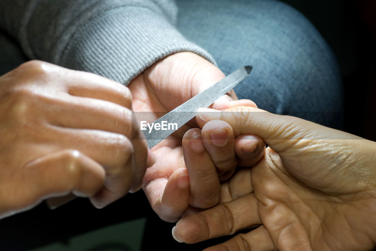 Cropped hands of woman filing customer fingernails at spa