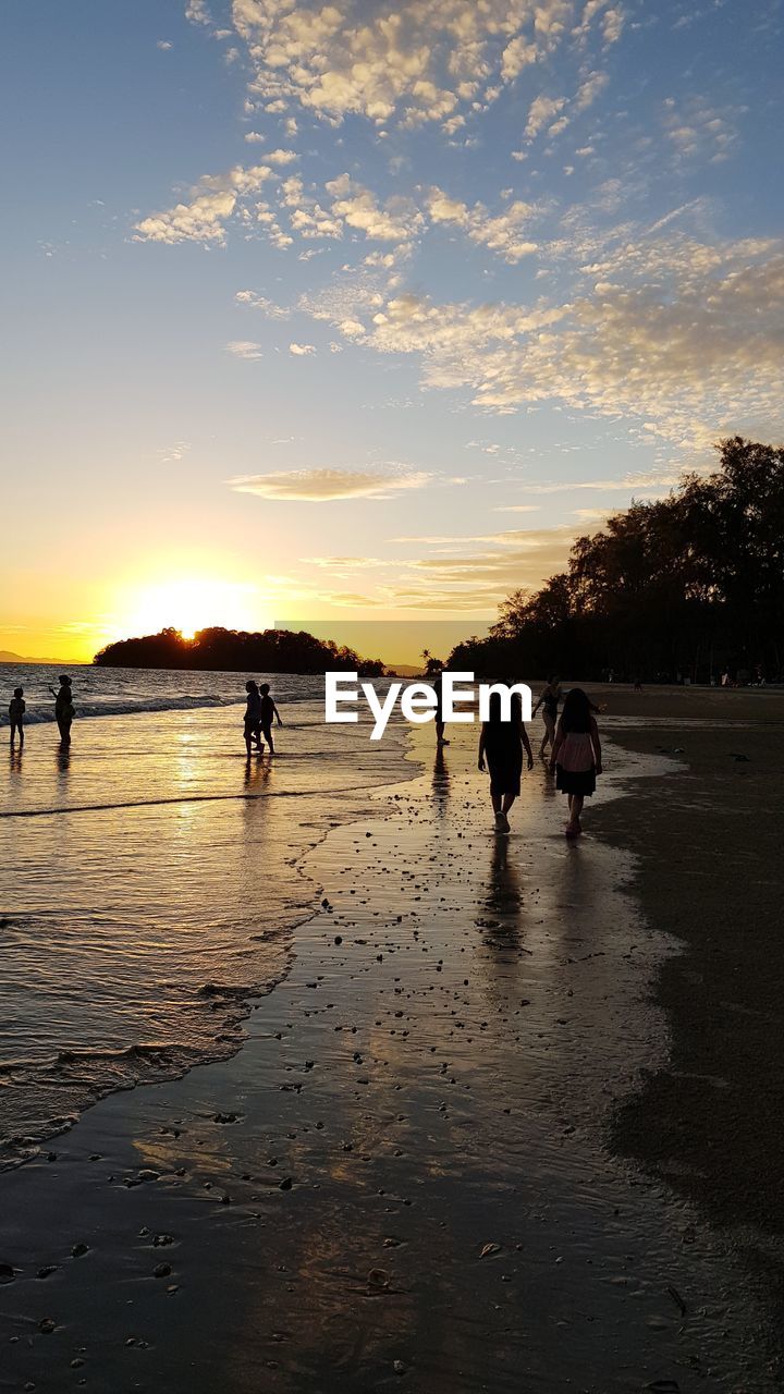 Silhouette people on beach against sky during sunset