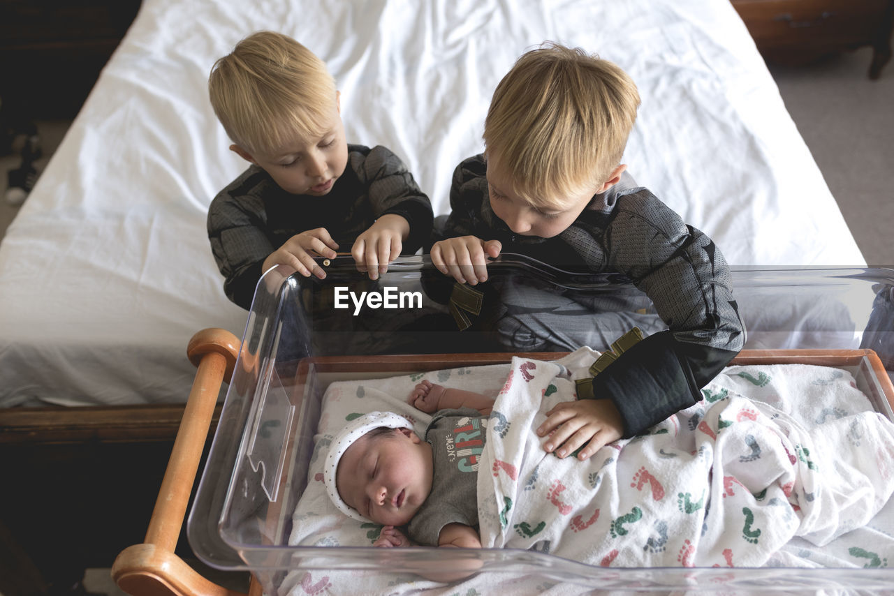 High angle view of brothers looking at baby girl sleeping in crib