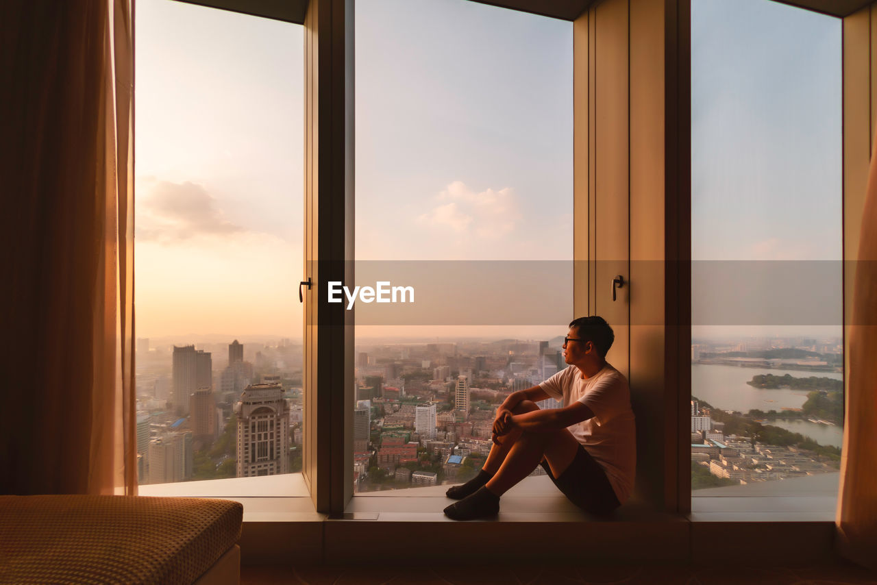 Man sitting on window sill during sunset