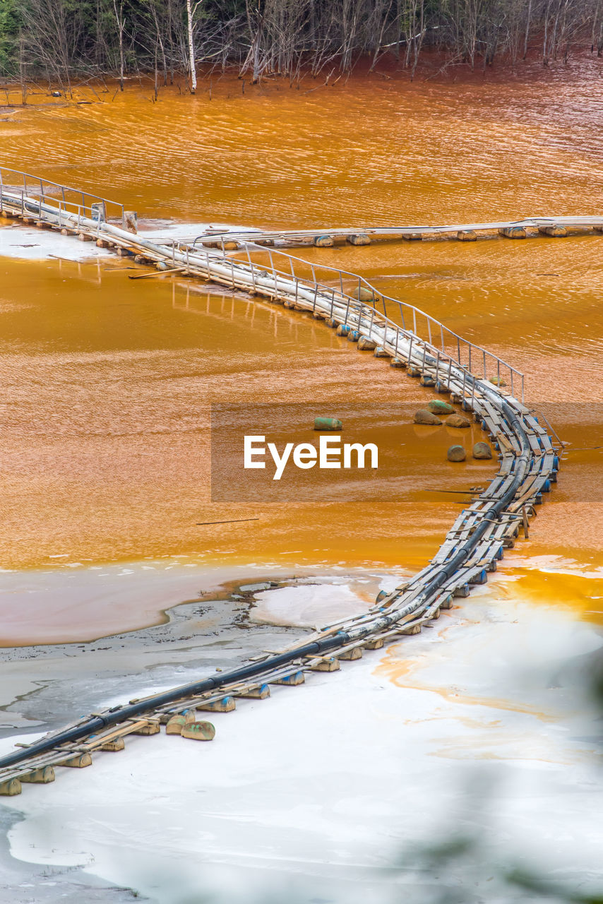 High angle view of pipe on bridge amidst dirty lake