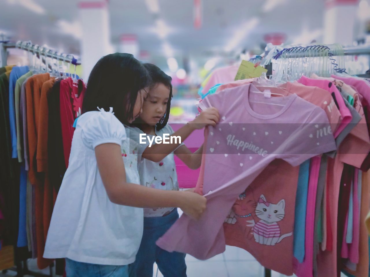 Little girls taking a look on beautiful children's clothes to choose at a supermarket.