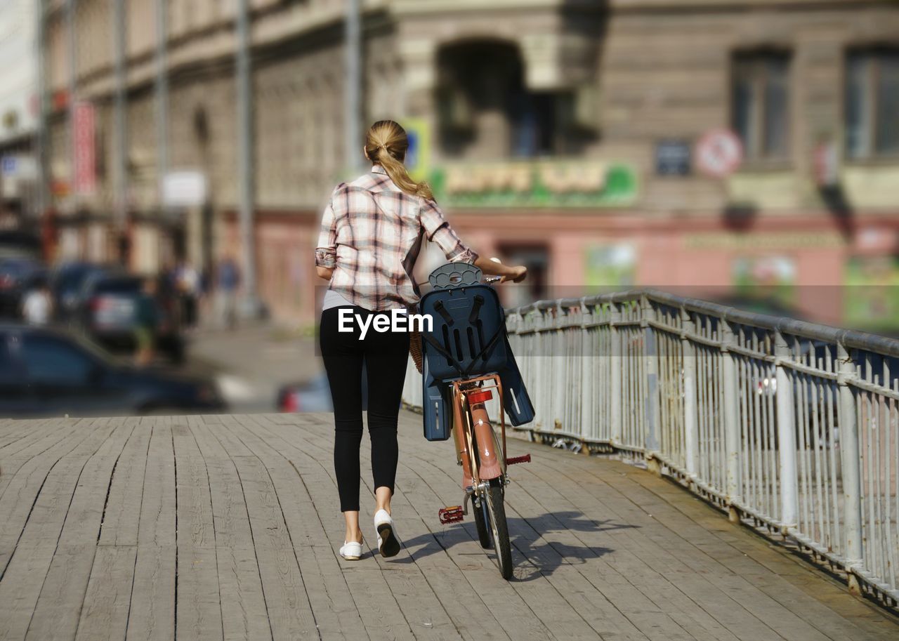 Rear view of woman with bicycle on wooden bridge during sunny day