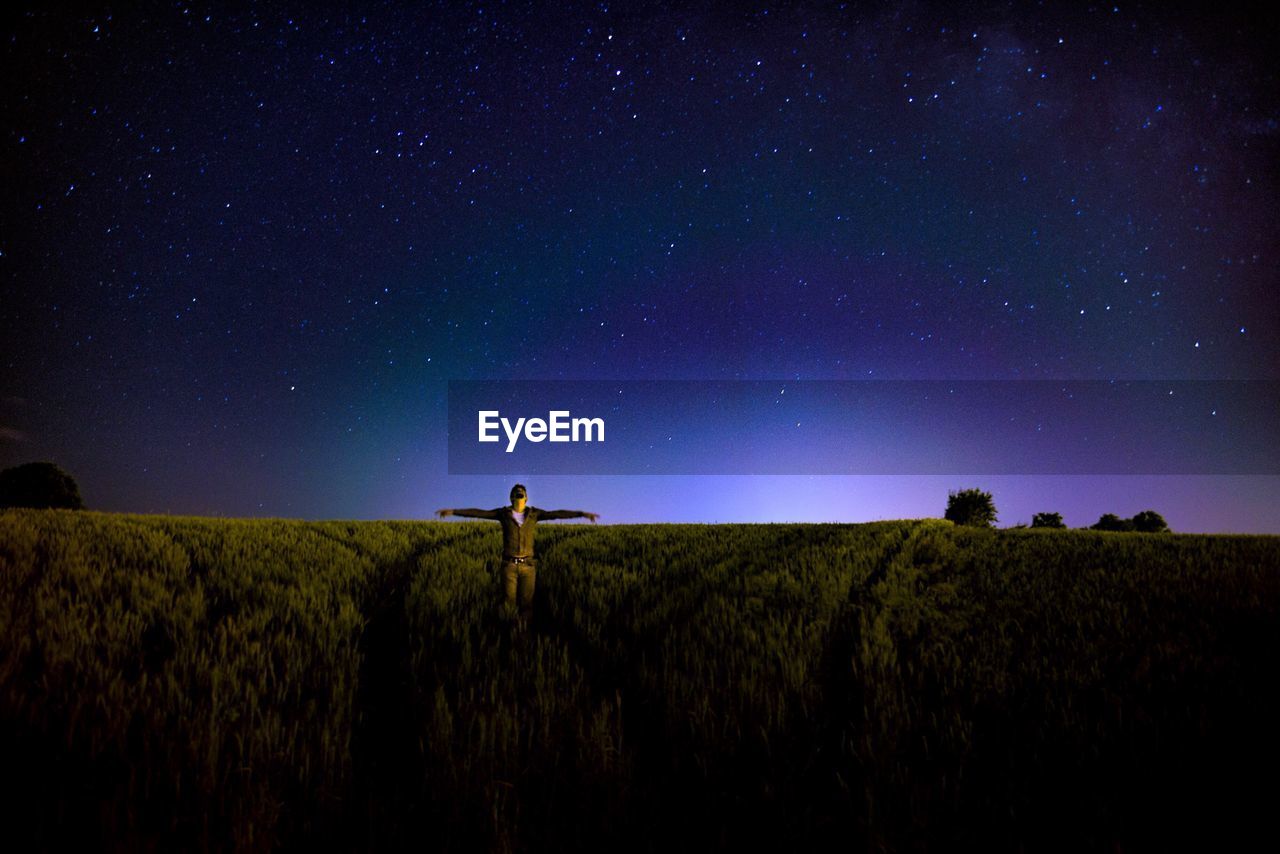 Man with arms outstretched standing on field against sky at night