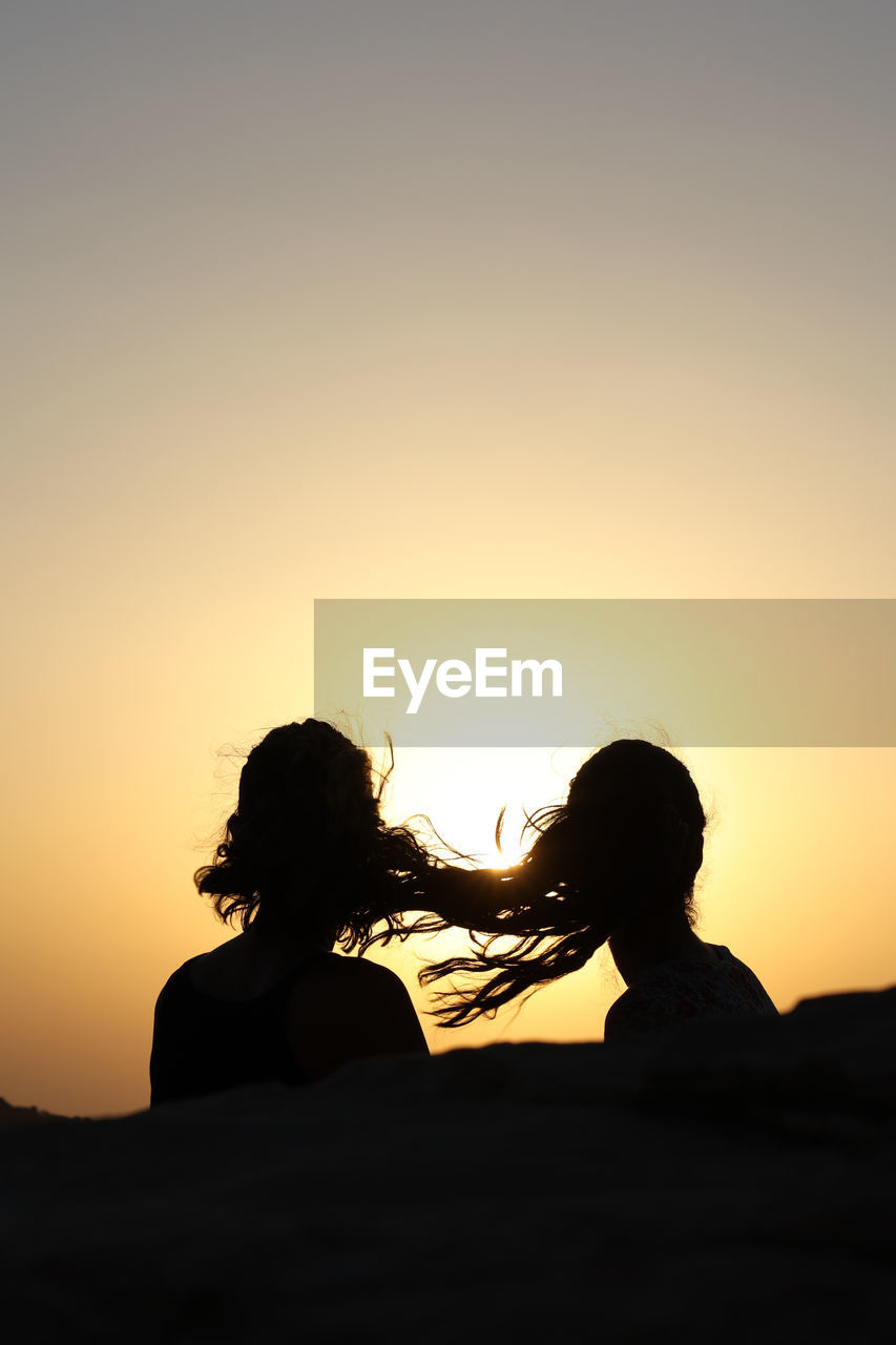 Silhouettes of two heads of young woman back with hair in the wind at sunset, copy space