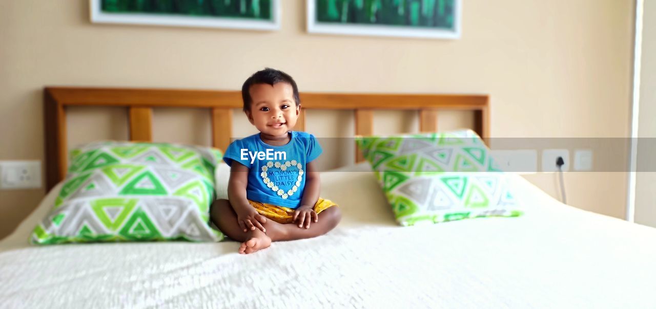 Cute smiling baby girl sitting on bed at home