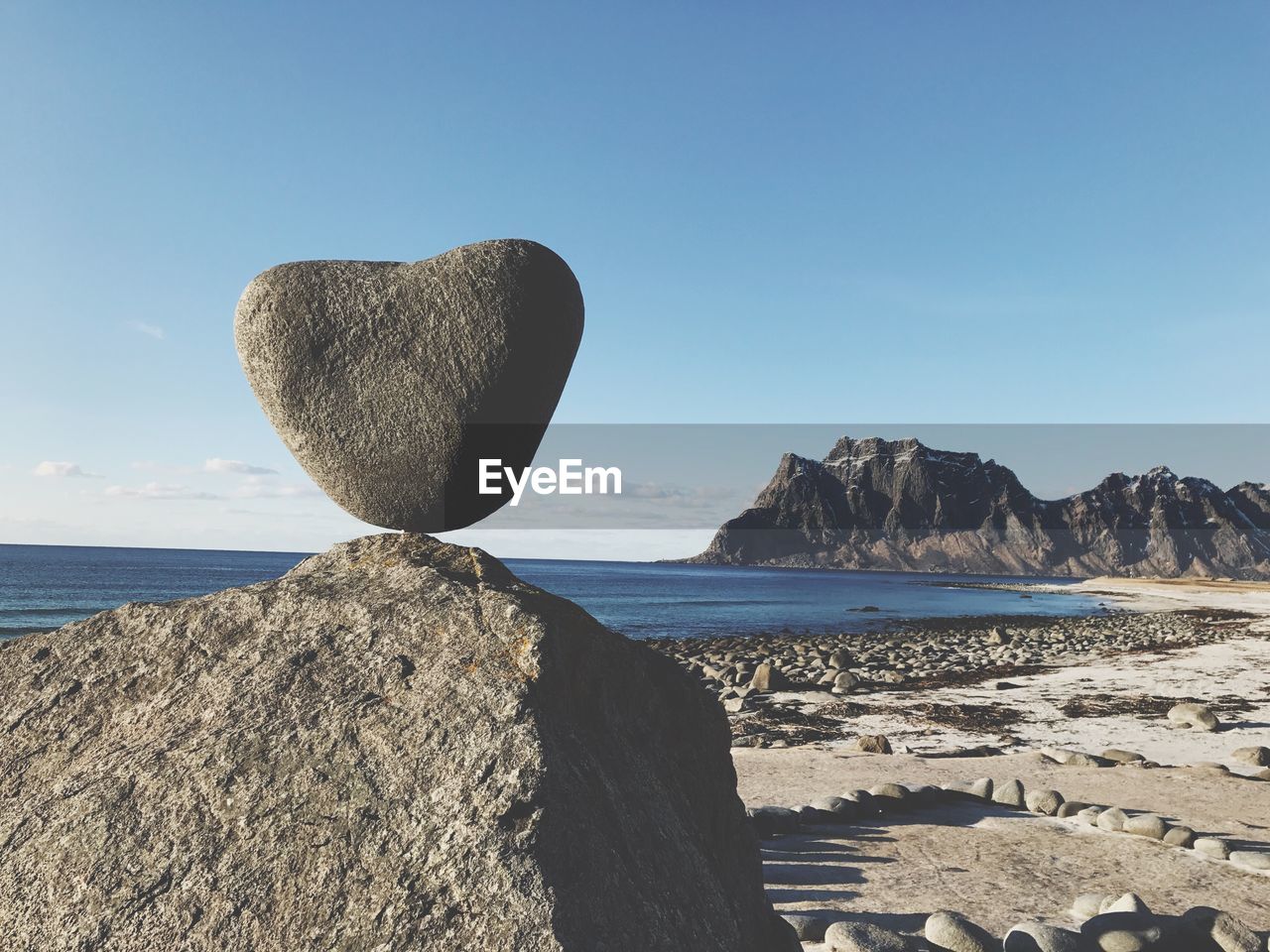 Heart shaped rock on beach against clear sky