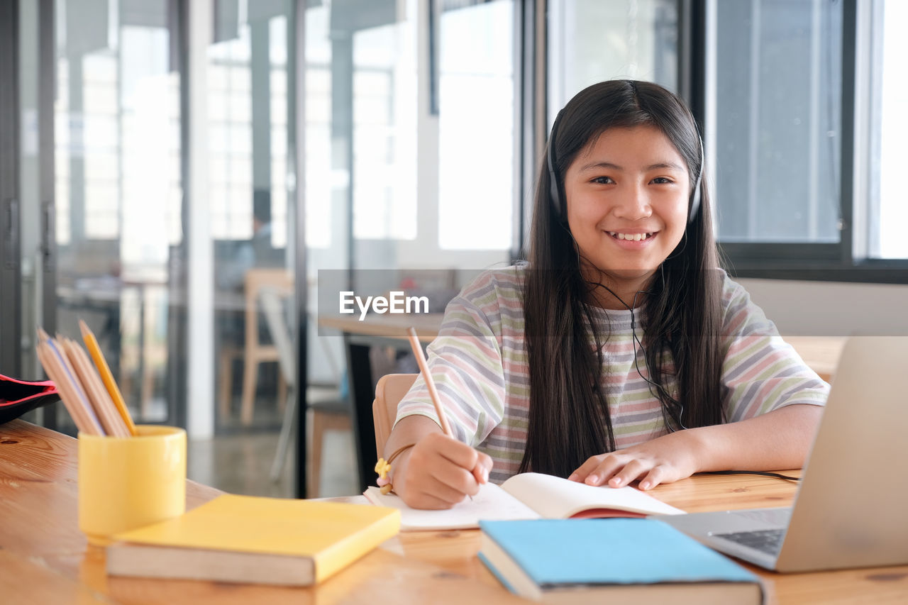 PORTRAIT OF SMILING YOUNG WOMAN SITTING AT TABLE