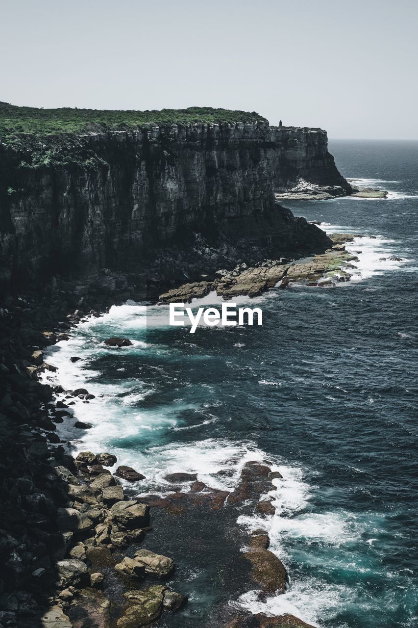 Scenic view of cliff by shore against sky