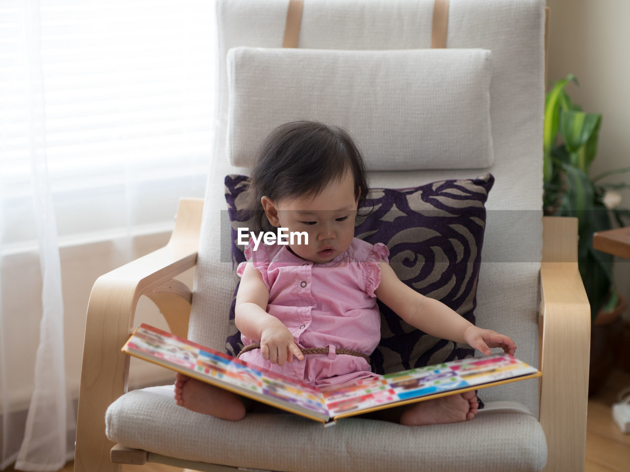 Cute girl sitting on chair and reading book at home