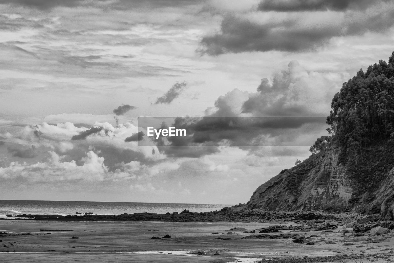 Scenic view of beach by cliff against sky