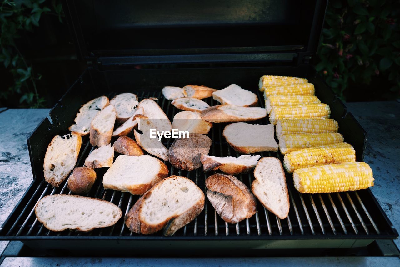 Bread slices and corns on barbecue grill at yard