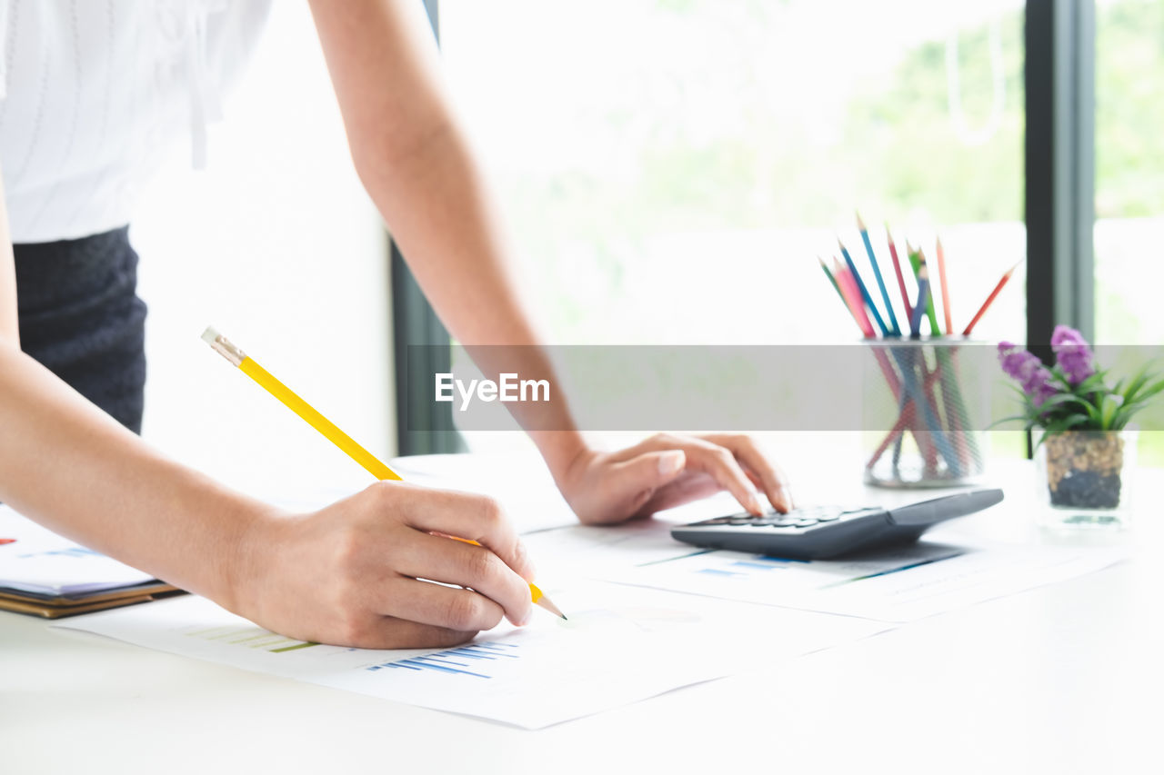 Midsection of businesswoman analyzing paperwork on table