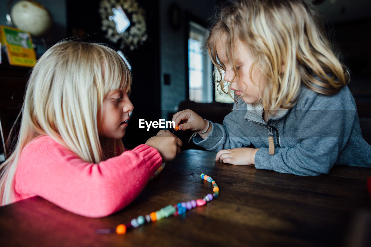 Little boy and girl making bead necklace at table during the day