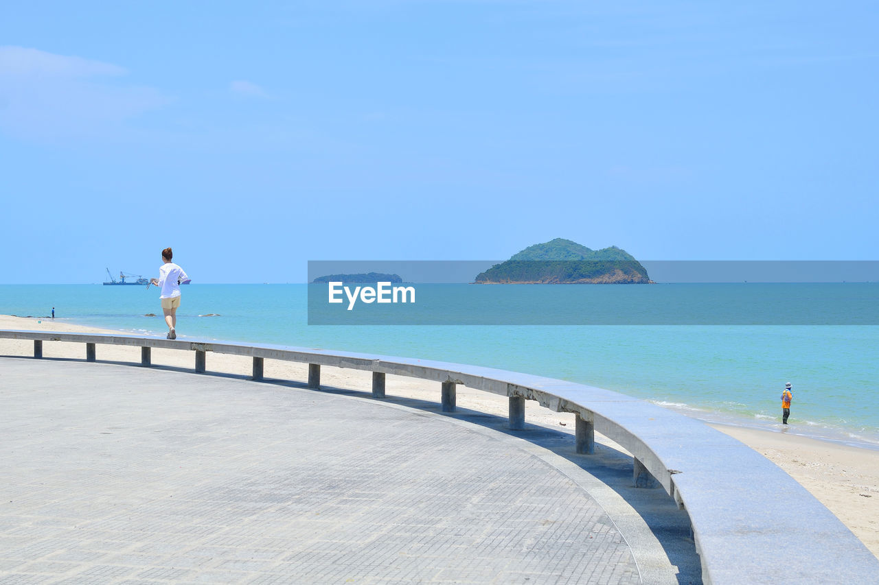 Rear view full length of woman walking on retaining wall at beach against sky