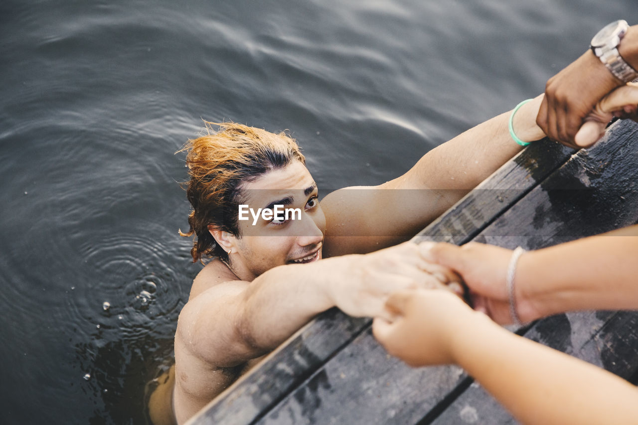 Cropped image of male friends holding hands with young man in lake