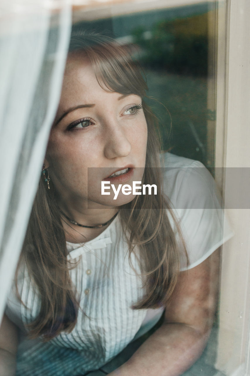 Thoughtful young woman looking through window