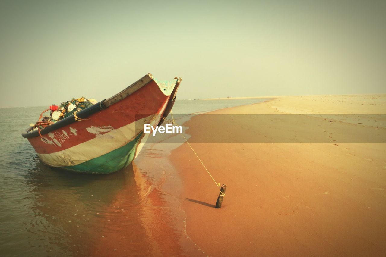 BOAT MOORED ON SHORE AGAINST SKY