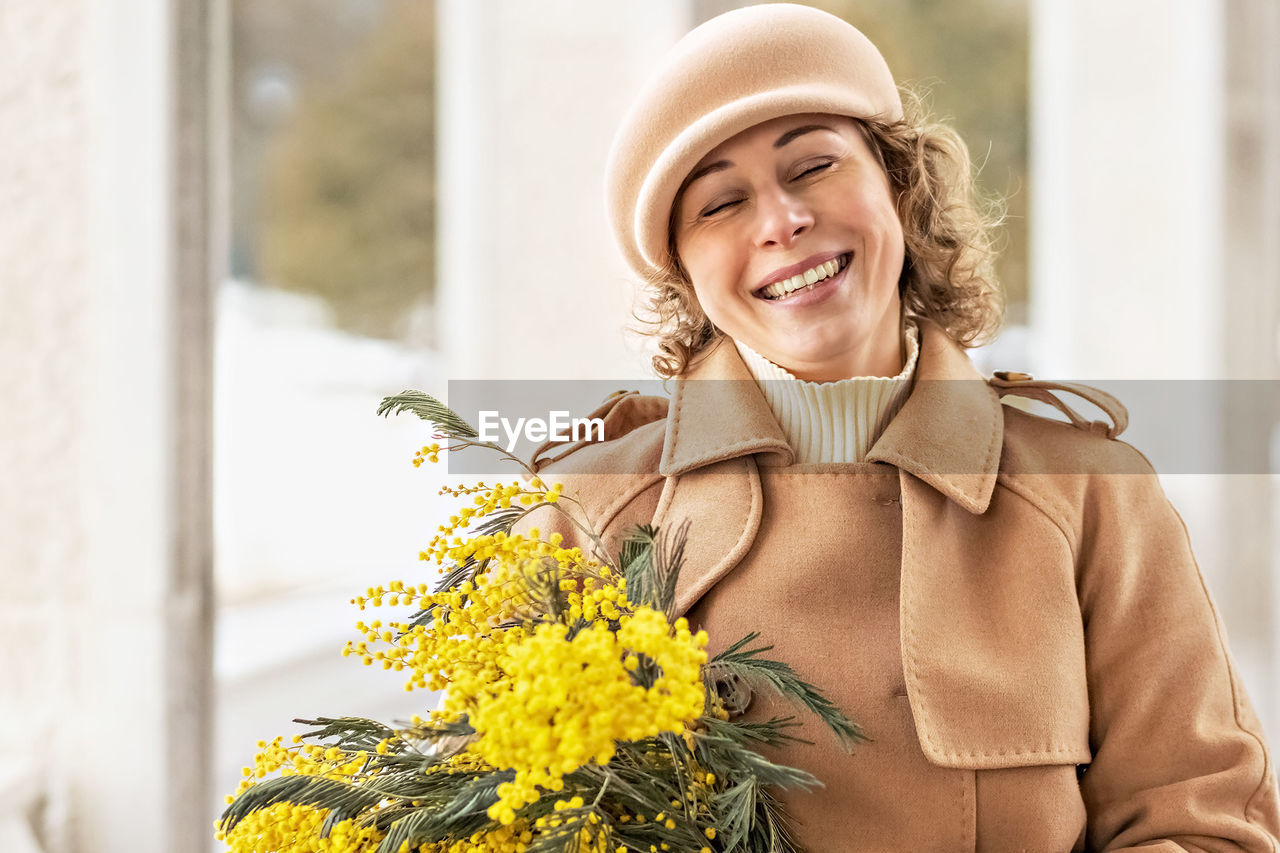 A young woman in a beige coat and hat with a bouquet of mimosa. international women's day