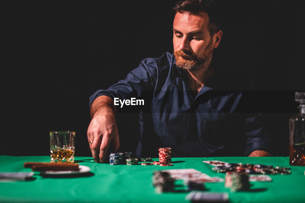 Man playing poker at table against black background