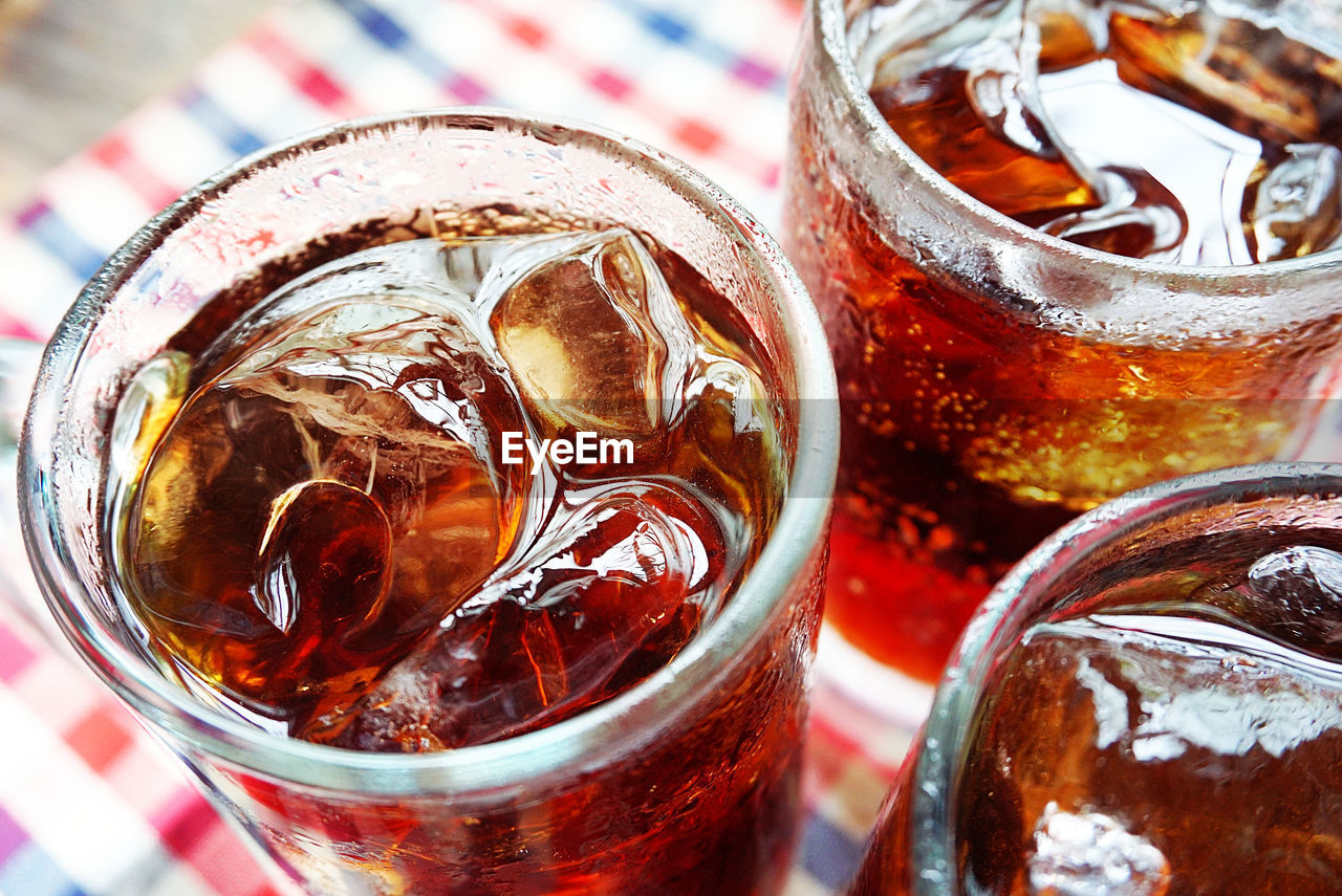 Three glasses of cola with ice on table cloth.