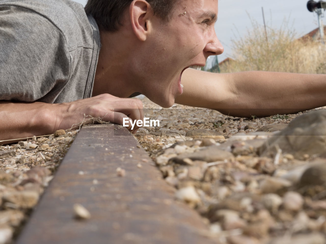 Close-up of man shouting while lying on railroad track
