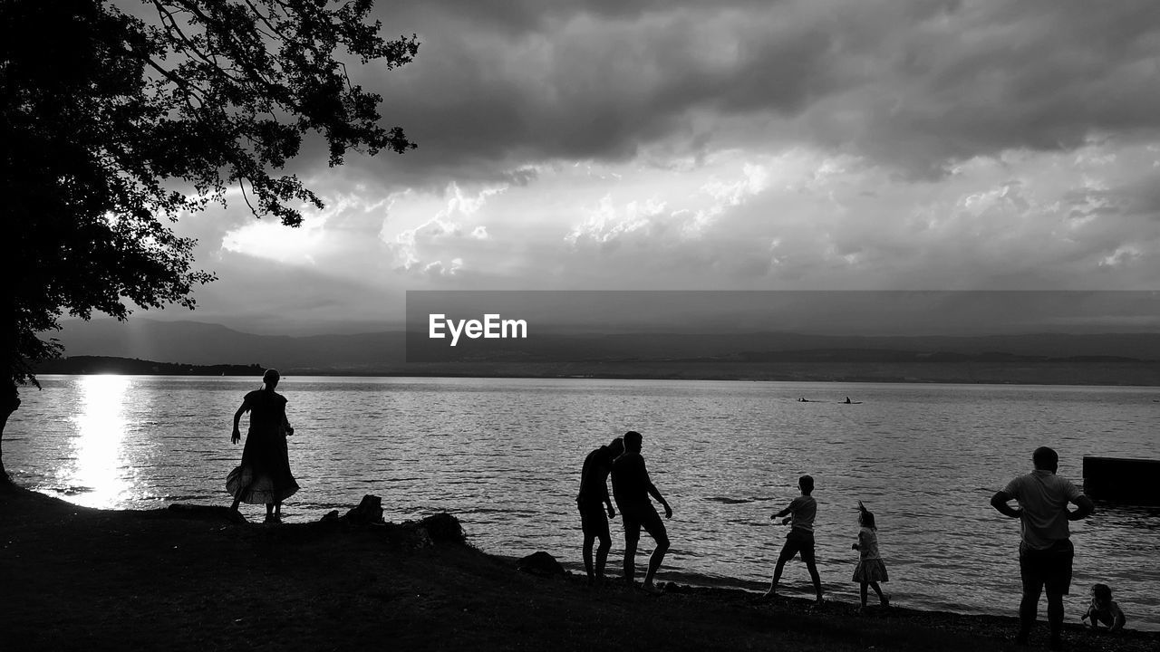 water, sky, sea, beach, black and white, cloud, monochrome, group of people, nature, monochrome photography, land, black, silhouette, horizon, beauty in nature, men, leisure activity, darkness, scenics - nature, lifestyles, adult, holiday, child, trip, vacation, childhood, women, tree, togetherness, outdoors, horizon over water, ocean, full length, white, person, environment