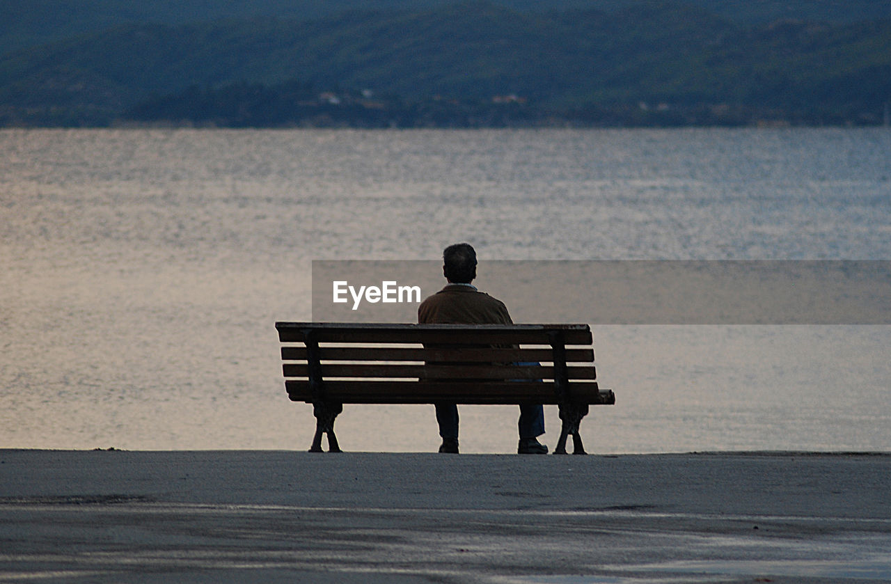 Rear view of man sitting on bench at beach
port, pyrgadikia, halkidiki, greece.