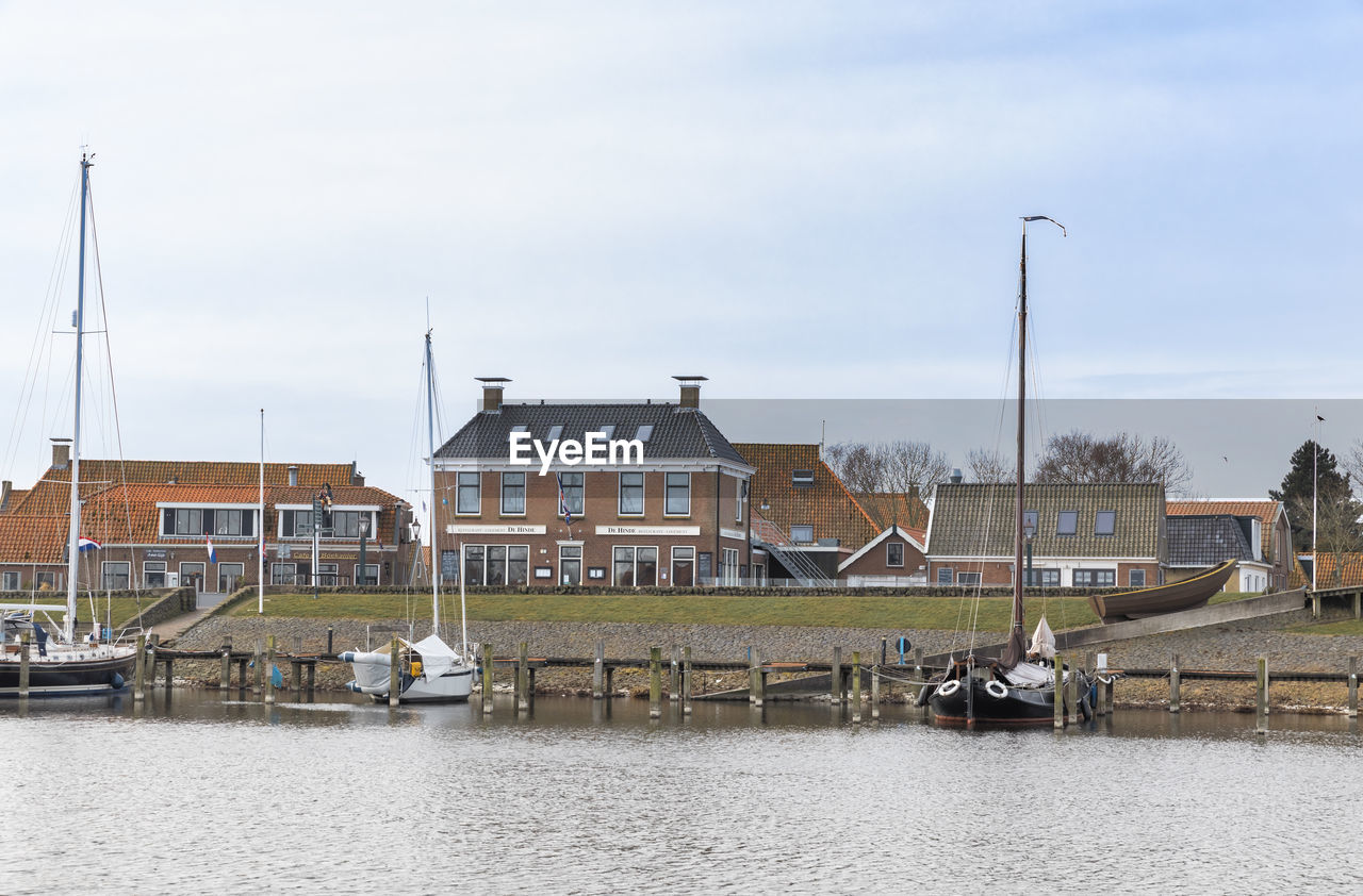 Sailboats in river by houses against sky