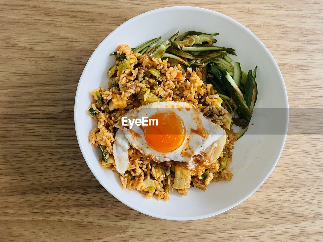 High angle view of food in plate on table, fried rice with egg on top and chopped cucumber