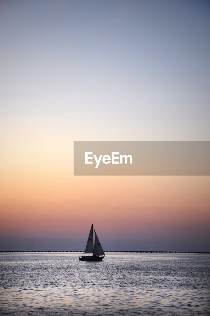 Sailboat sailing on sea against sky during sunset