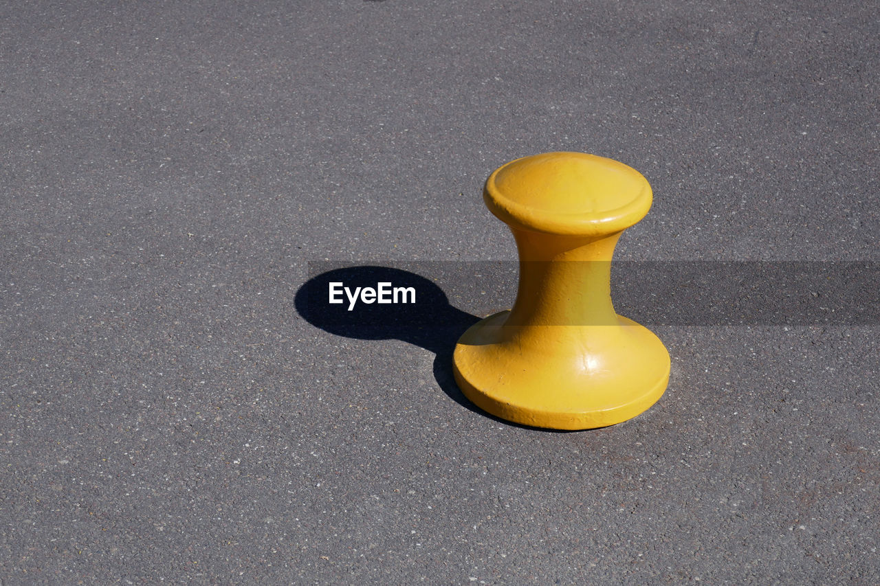 High angle view of yellow bollard with shadow on street