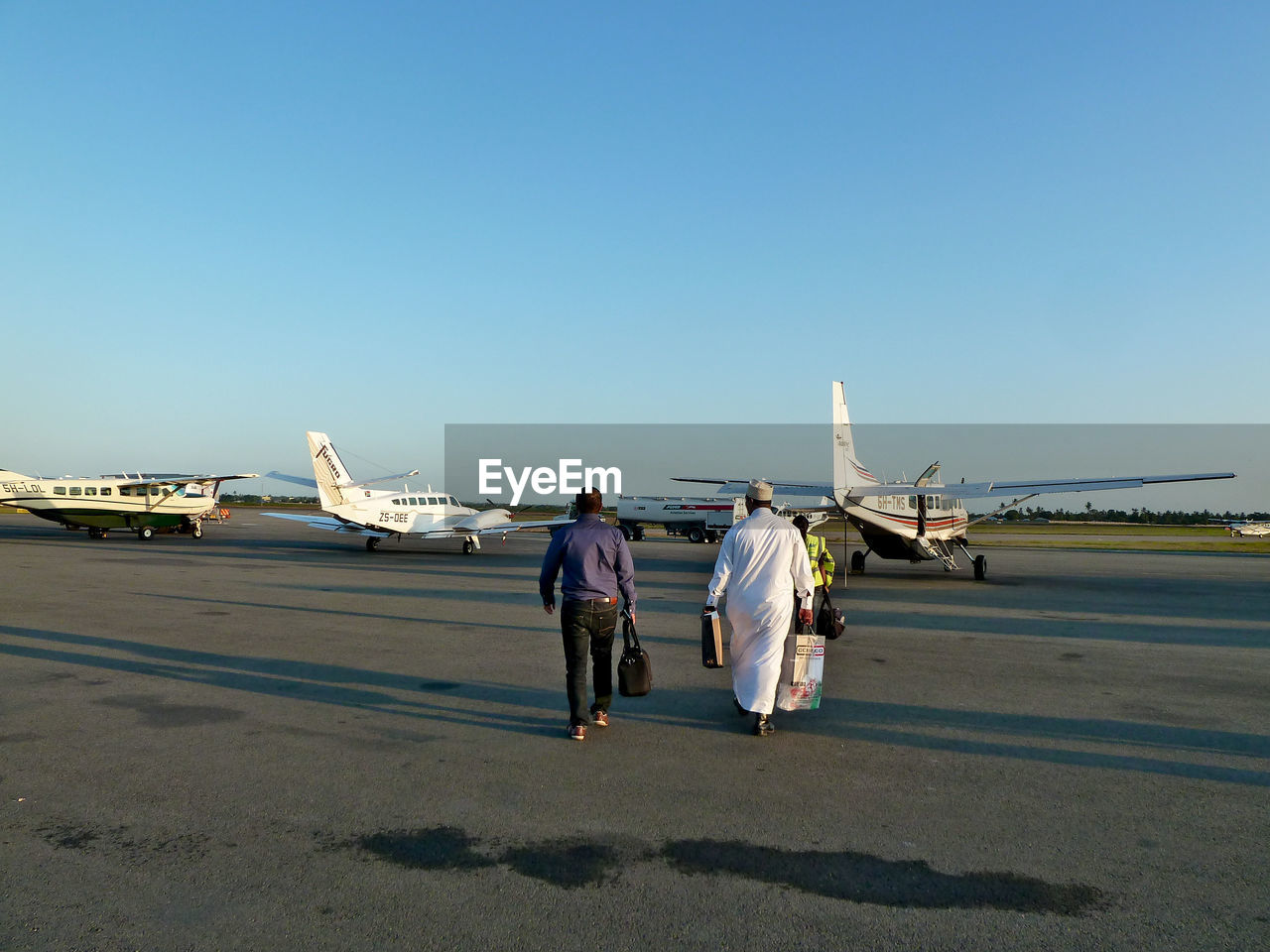 Rear view of people walking at airport runway against clear sky