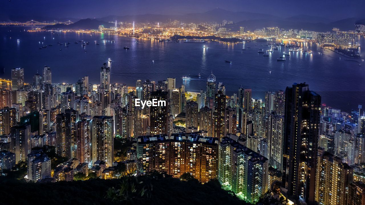 High angle view of illuminated modern buildings by lake in city at night