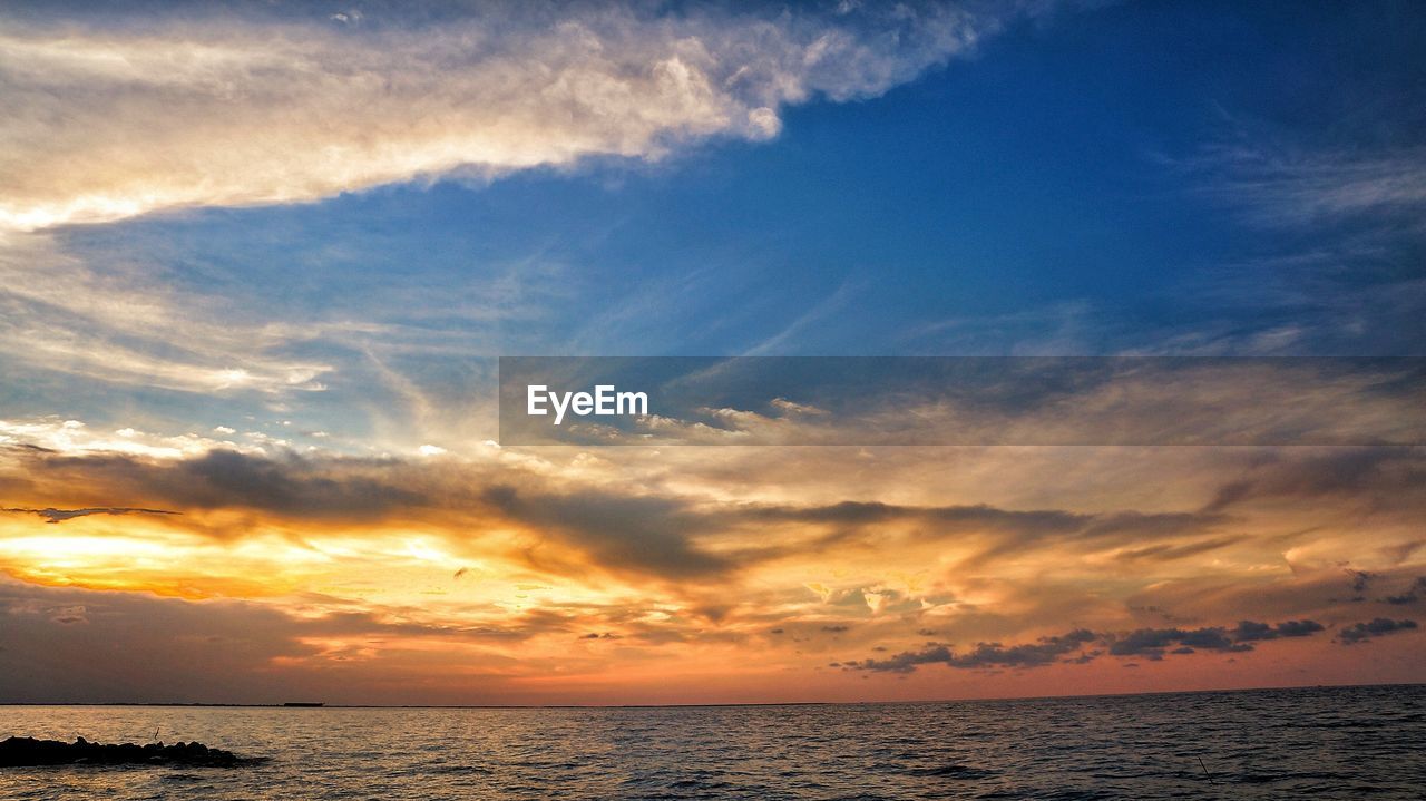 Scenic view of sea against dramatic sky during sunset