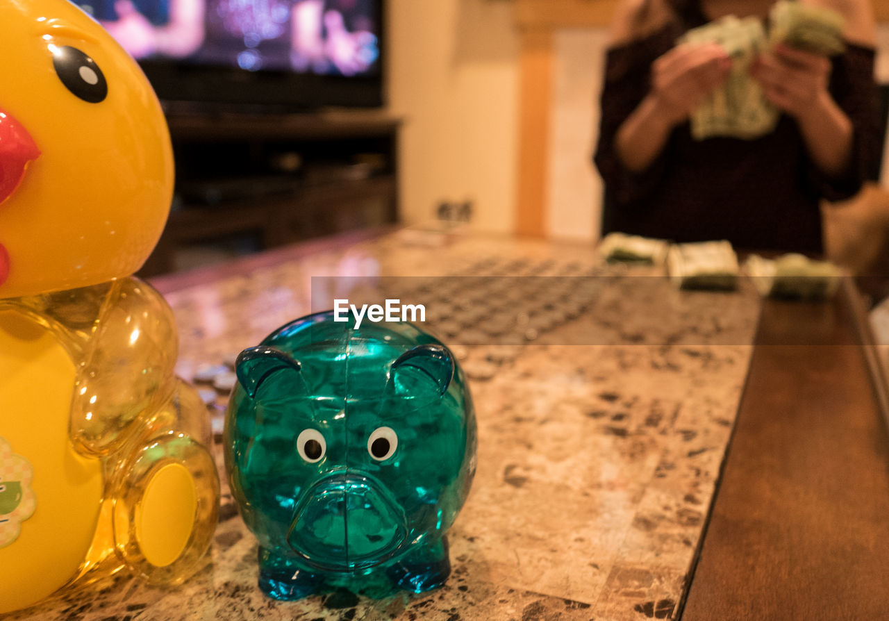 Piggy bank on table with person counting currency in background at home