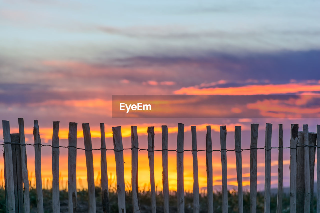 Fence on landscape against romantic sky at sunset