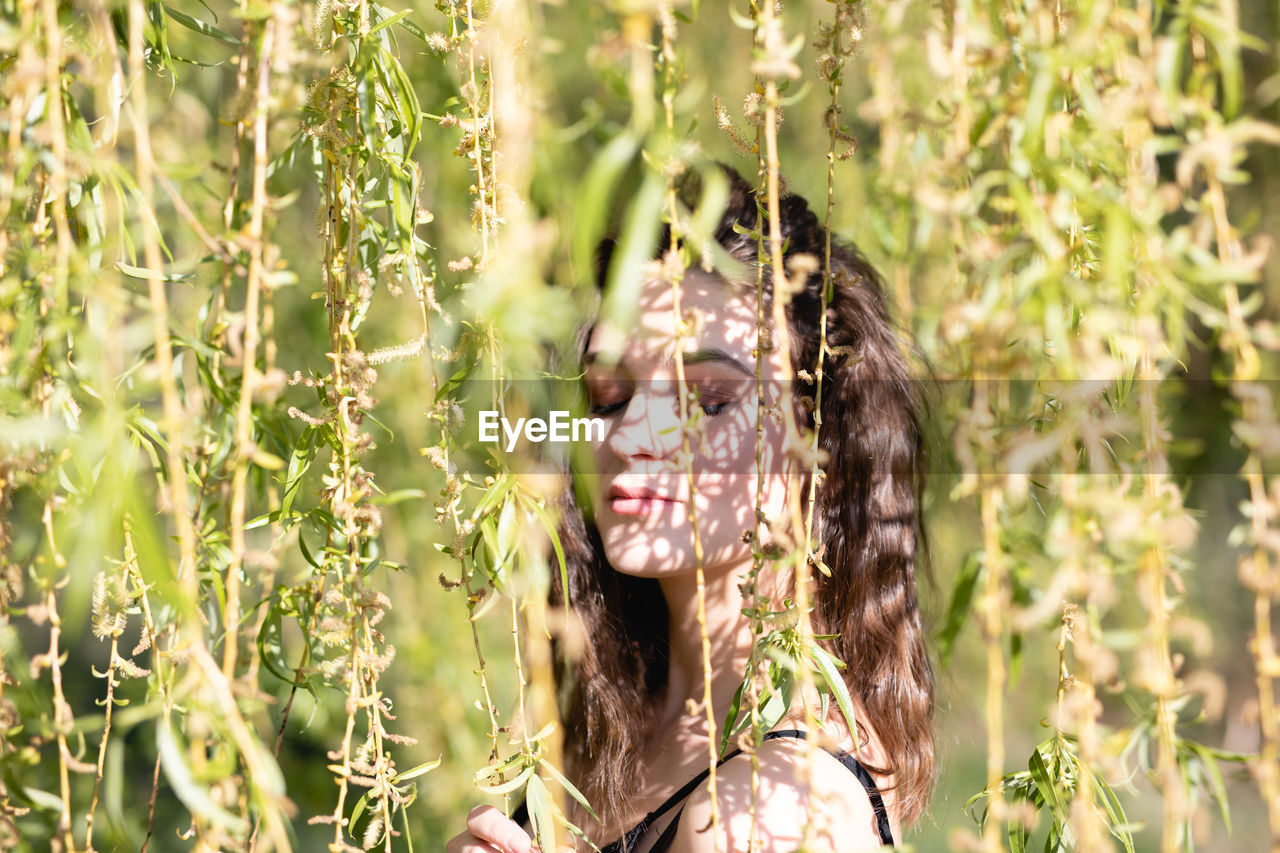 Side view of woman with eyes closed standing by plants in park