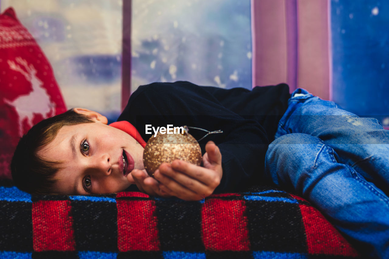 Caucasian blond boy lying down holding a christmas toy looking at camera. merry christmas