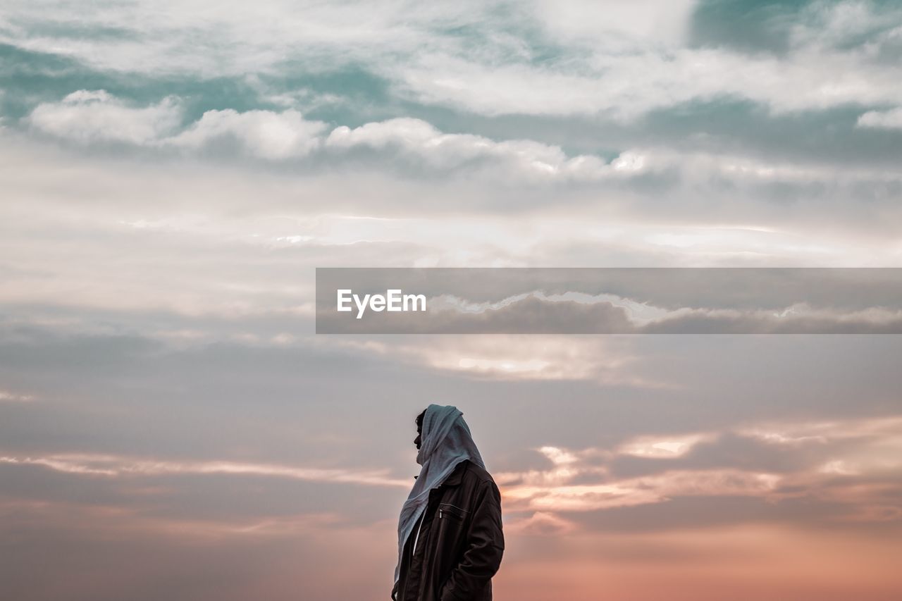 MIDSECTION OF WOMAN STANDING AGAINST SKY DURING SUNSET