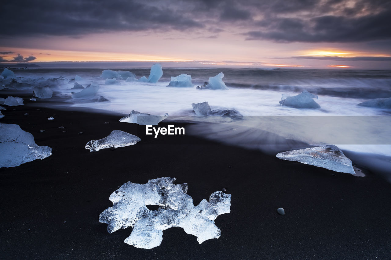 Ice at beach against sky during sunset