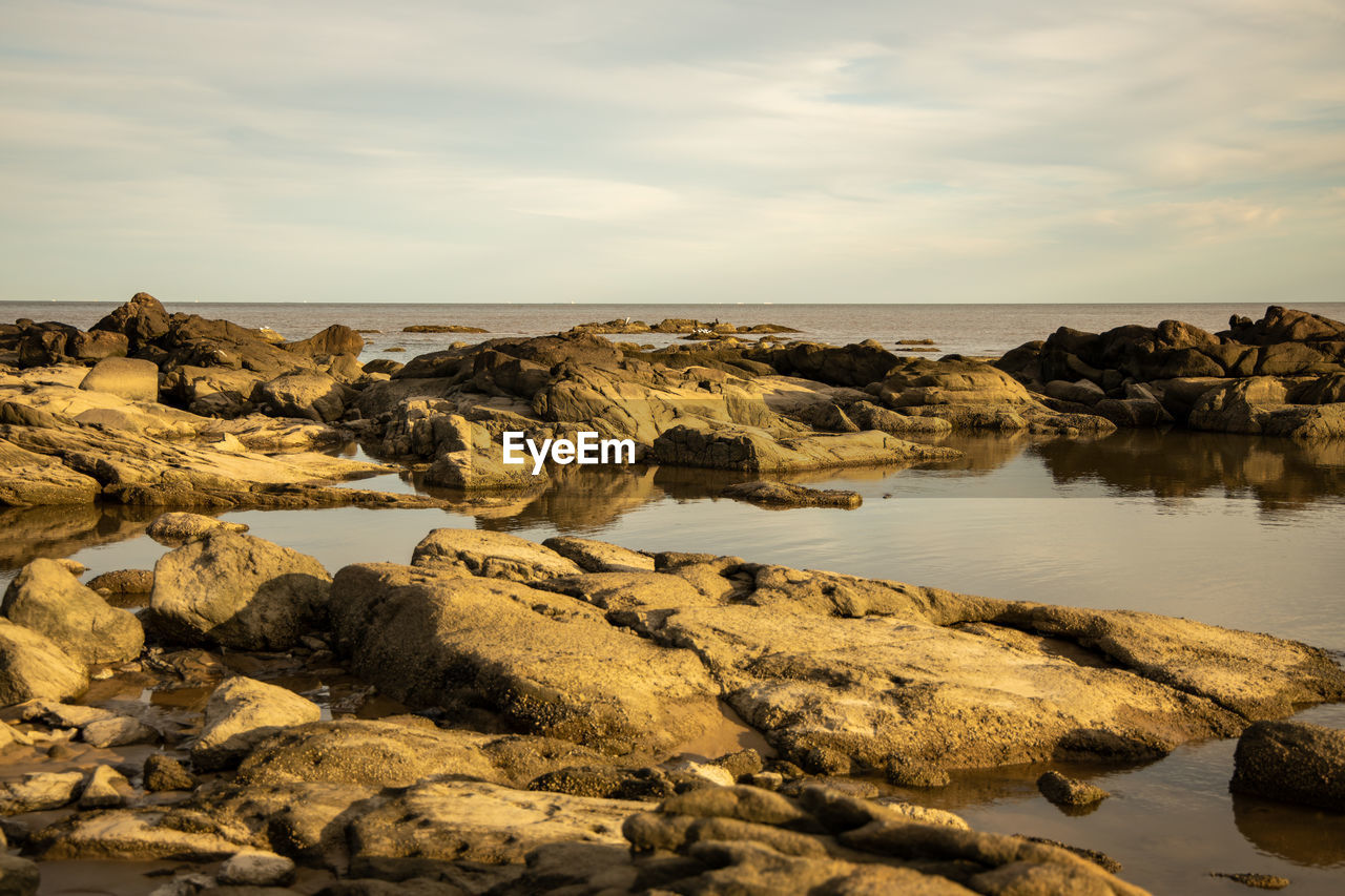 Scenic view of rocks by sea against sky