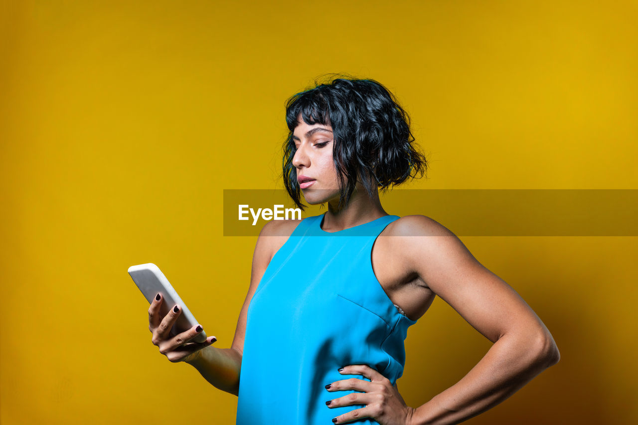 Young woman using mobile phone against yellow background