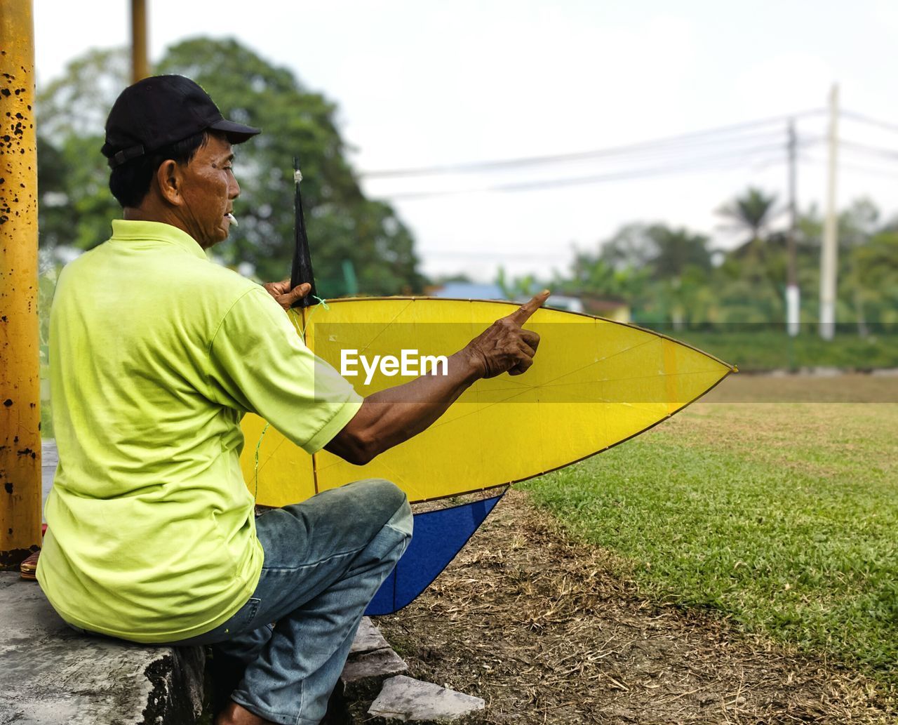 Man with kite pointing while sitting against sky