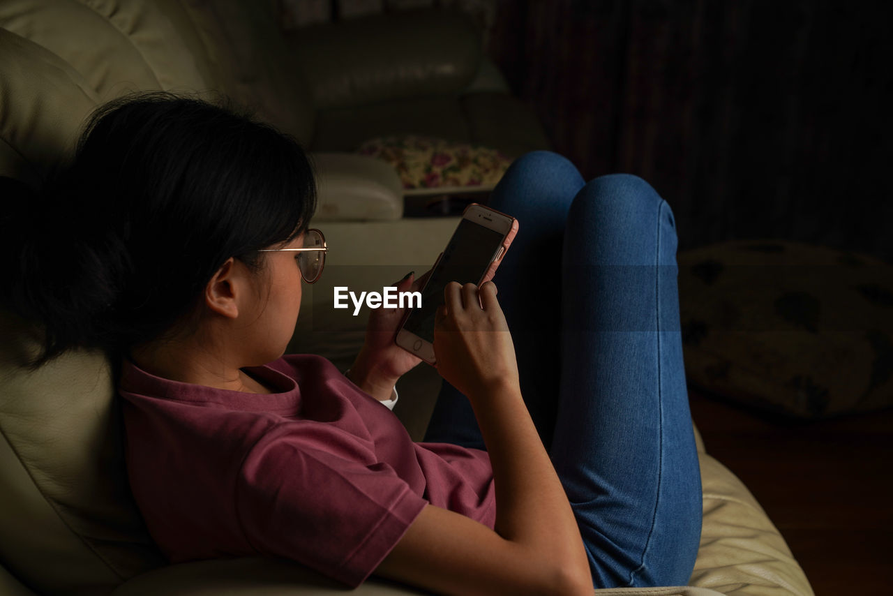 REAR VIEW OF WOMAN USING MOBILE PHONE IN BEDROOM