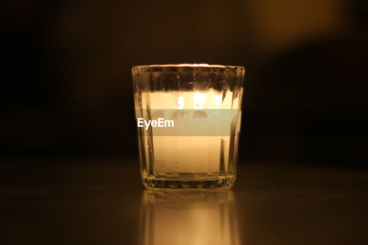 CLOSE-UP OF GLASS CANDLE ON TABLE AGAINST BLACK BACKGROUND