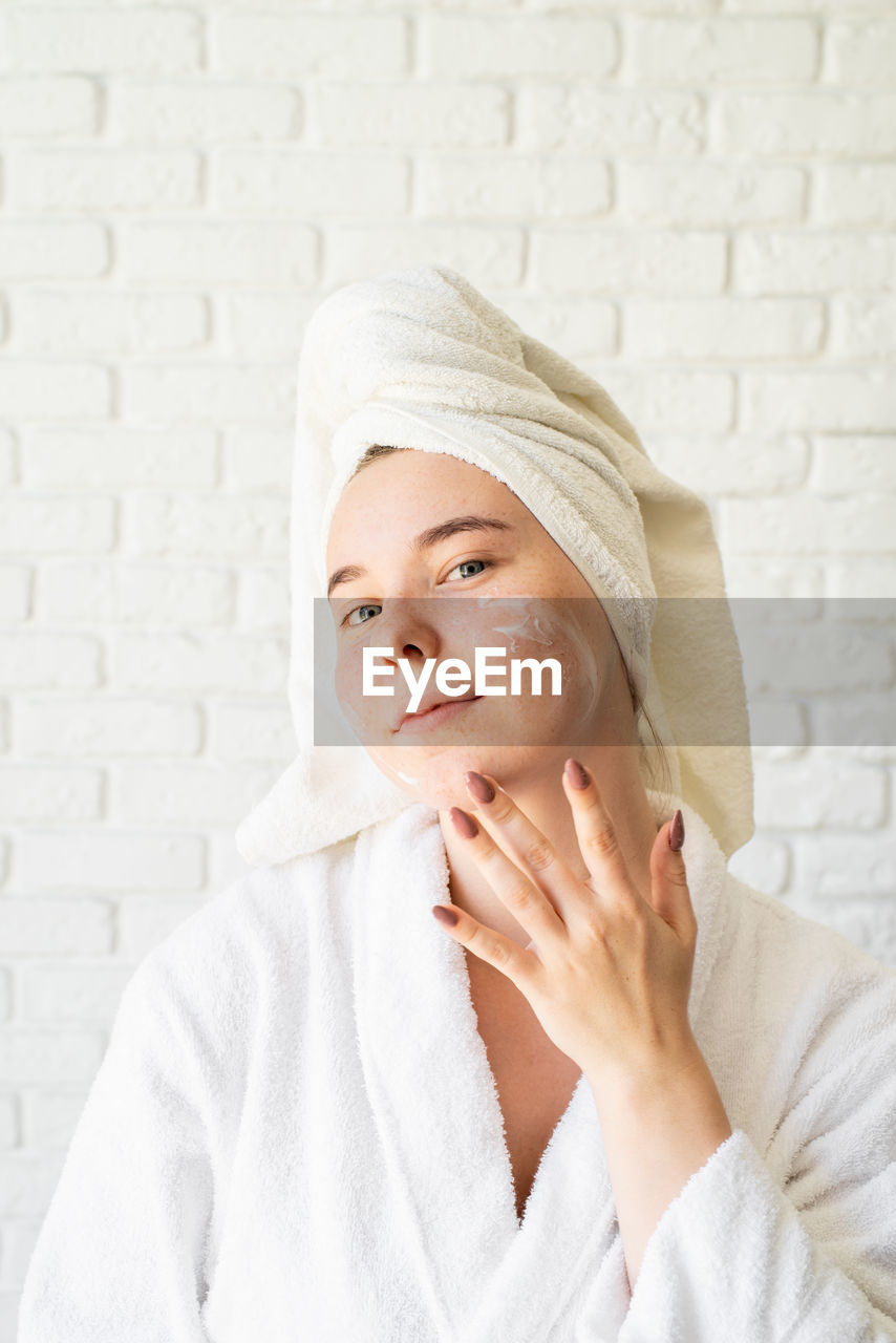 Spa and beauty. young smiling woman wearing white bath towels with a clay facial mask on her face