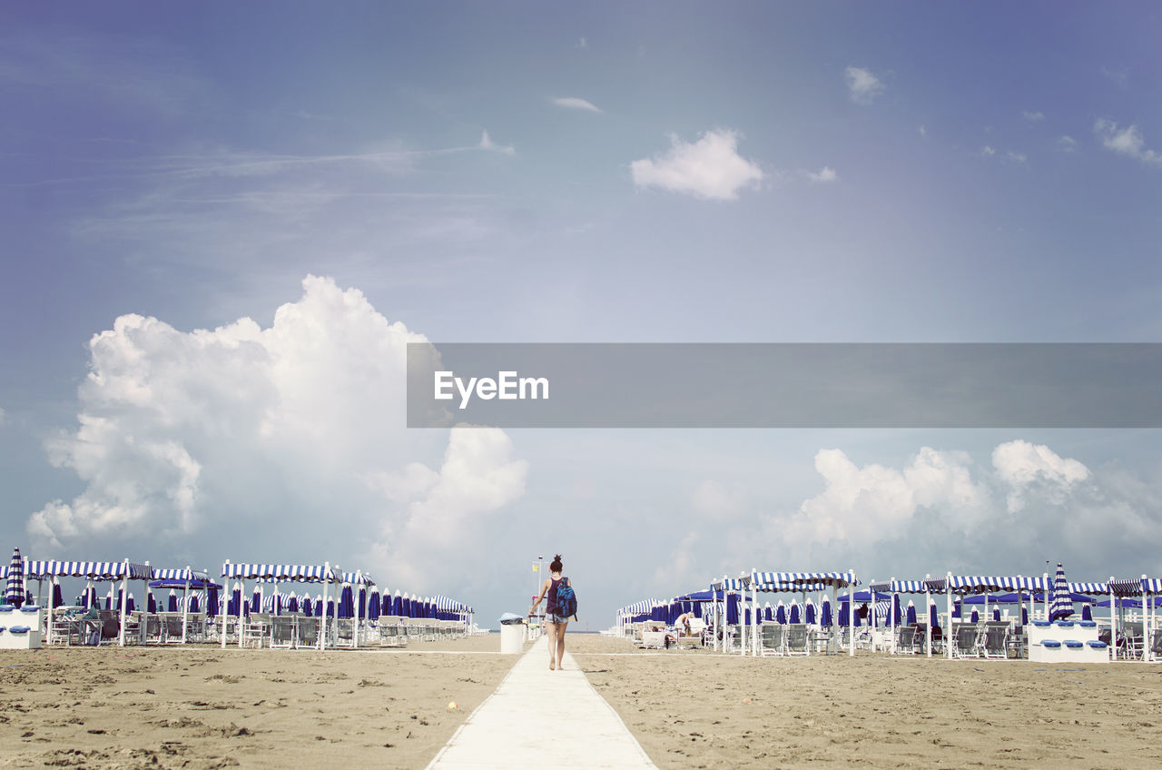 Rear view of woman walking on footpath amidst sand at beach