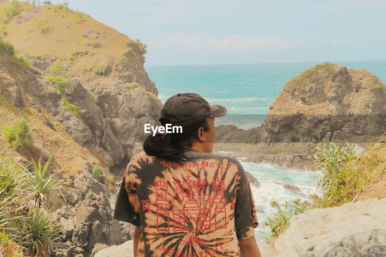 Rear view of man looking at sea shore against sky