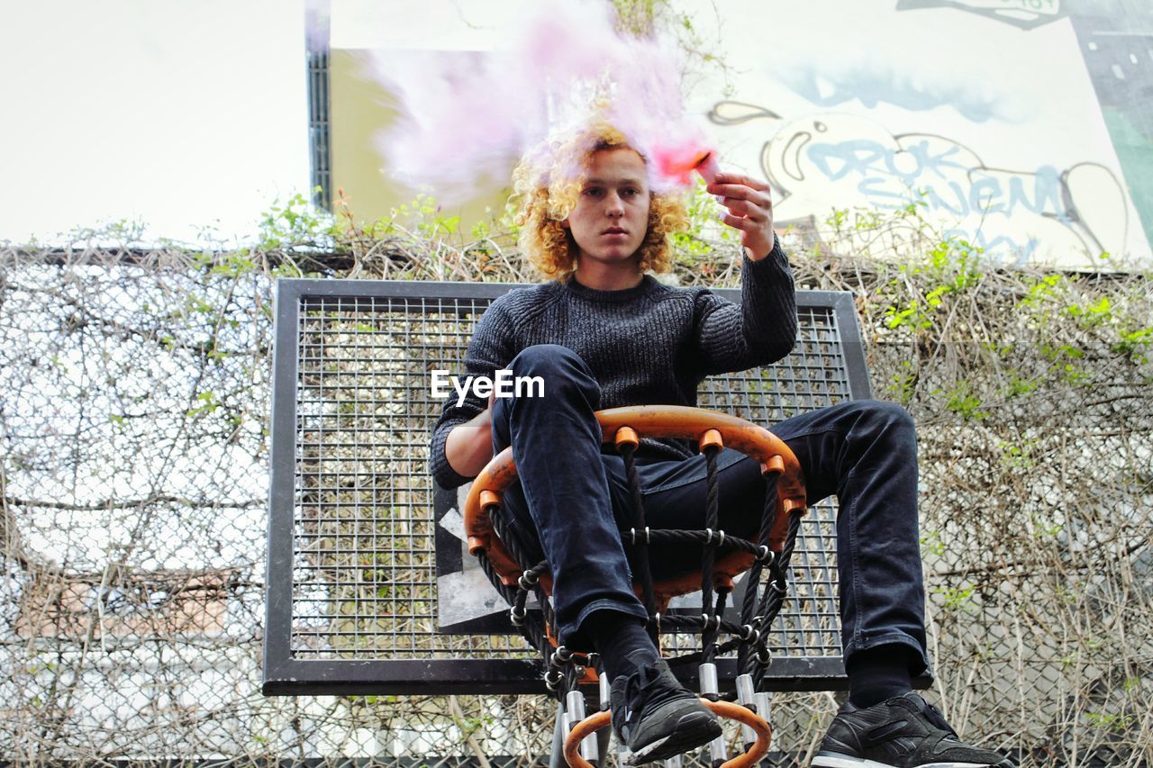 PORTRAIT OF YOUNG MAN SITTING ON TABLE AGAINST BUILDING